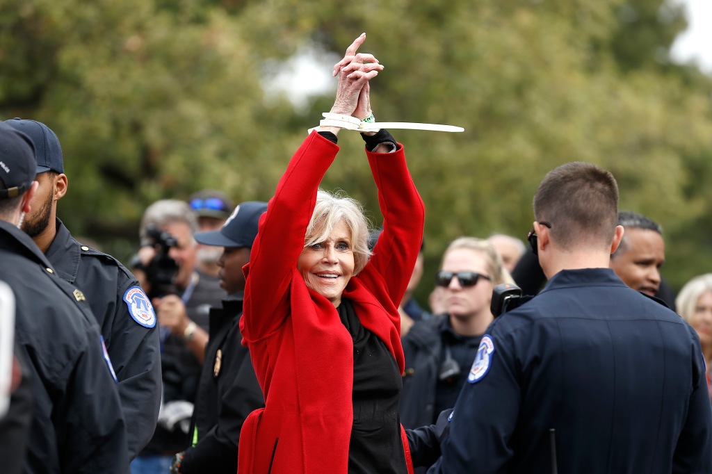 Jane Fonda in zip tie handcuffs while wearing red jacket at protest