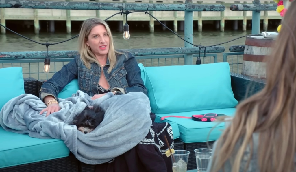 A blonde woman sitting on a rooftop bar cloth chair. 