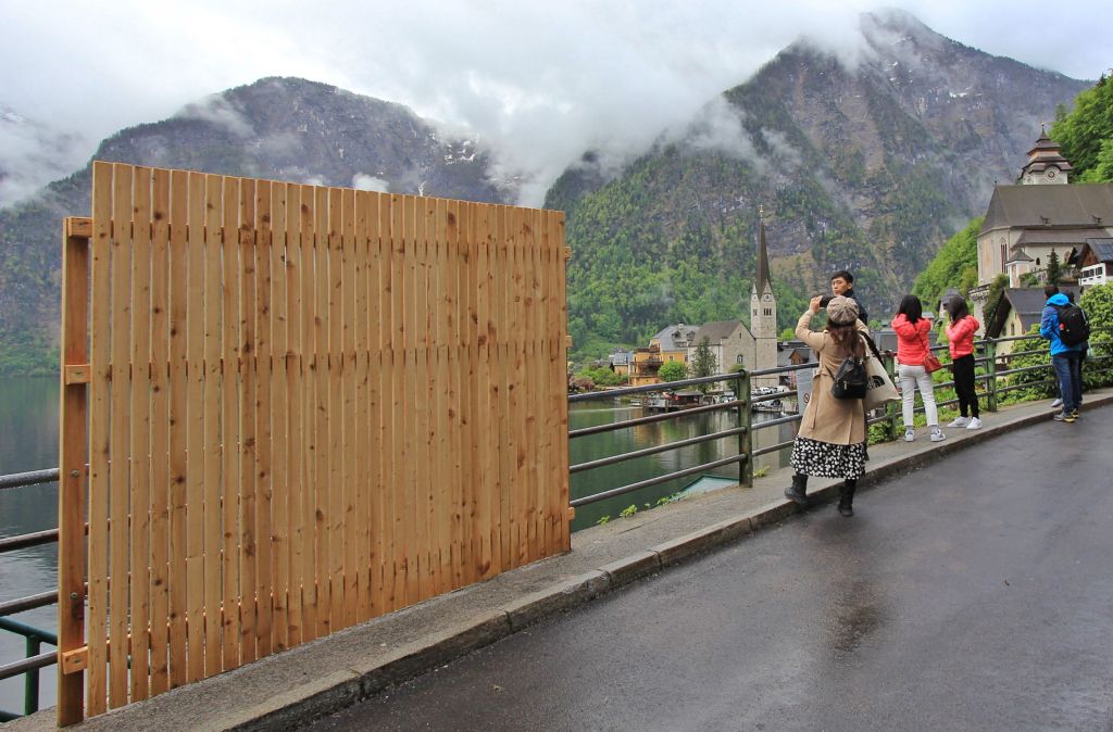 A provisional wooden fence is partially blocking the beautiful view, as visitors take selfies with the landscape.