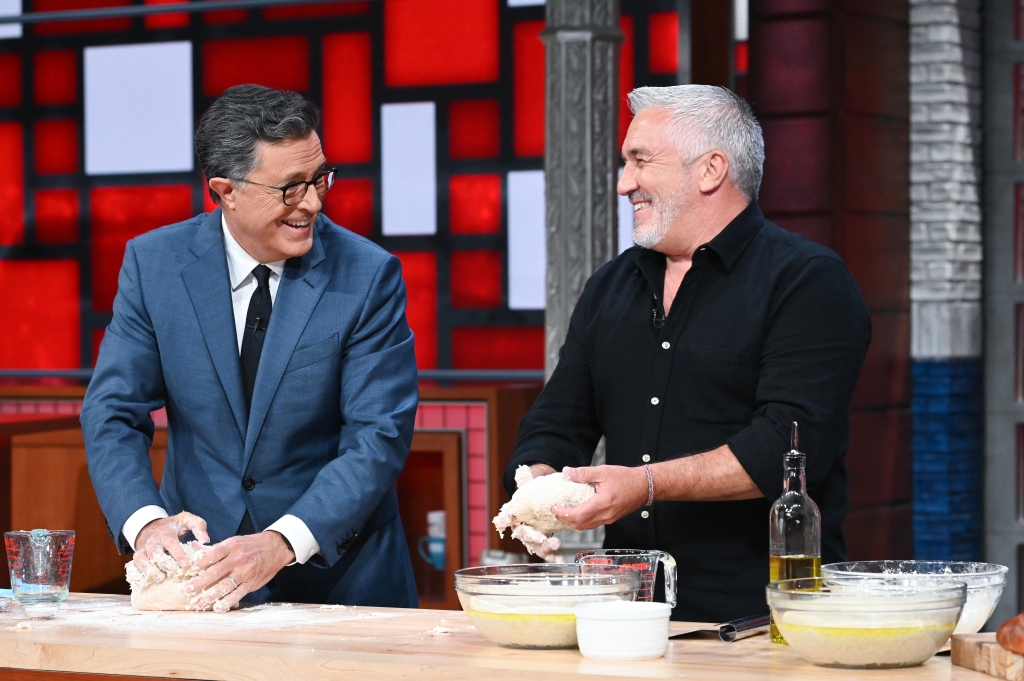 Paul Hollywood smiling holding dough with Stephen Colbert. 