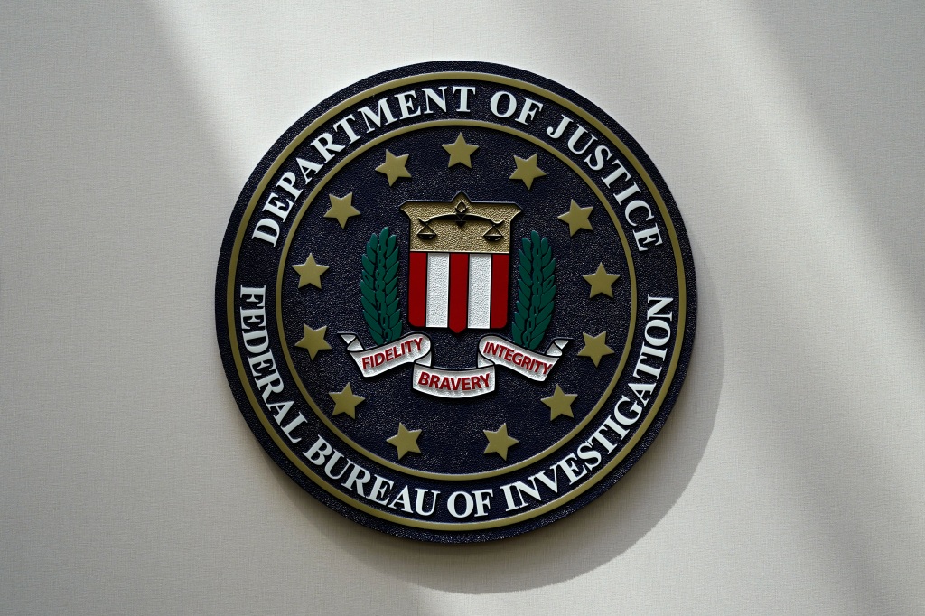 A wall plaque of the FBI's emblem reading "Department of Justice - Federal Burau of Investigations"