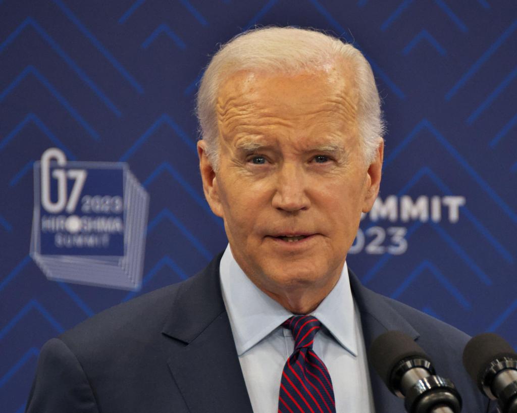 President Joe Biden stands in a suit in front of microphones at the G7 Summit