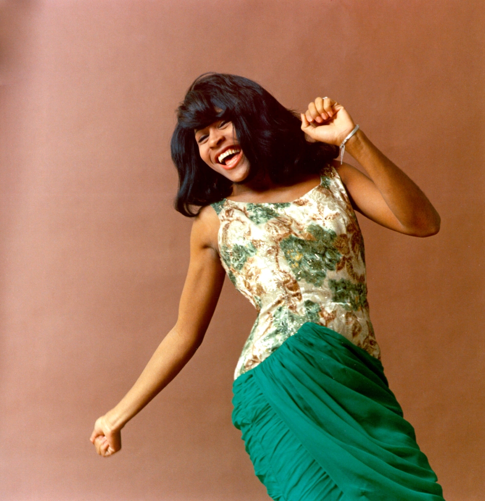 Photographed in 1964, Tina Turner looks joyful while dancing in a portrait wearing a green floral dress