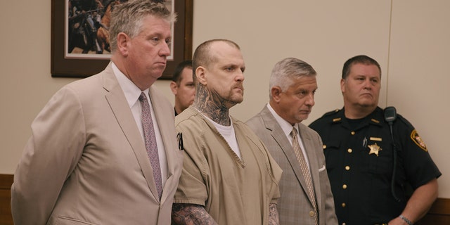 Michael Siager standing up in a beige jumpsuit during trial