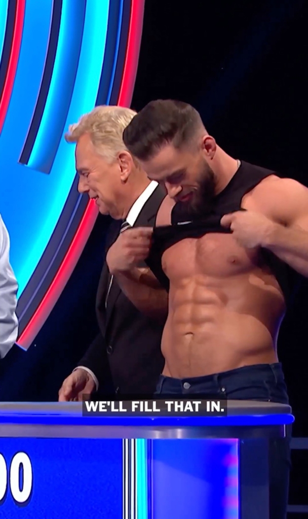 Sajak with WWE star and "Wheel of Fortune" contestant Austin Theory, who's lifting up his shirt as Sajak looks away and smiles.