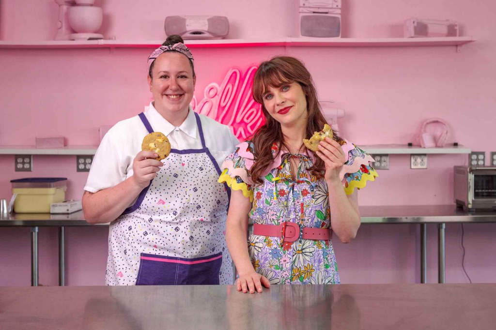 Zooey Deschanel posing with Anna McGorman from Milk Bar. They're both smiling and looking at the camera and both are holding cookies.