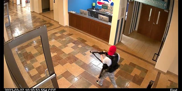 Audrey Hale wears red hat and carries guns as she walks through school hallways