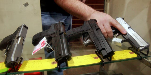 man holding gun that's in display case with other guns