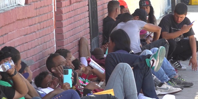 A row of migrants lay against a brick wall waiting