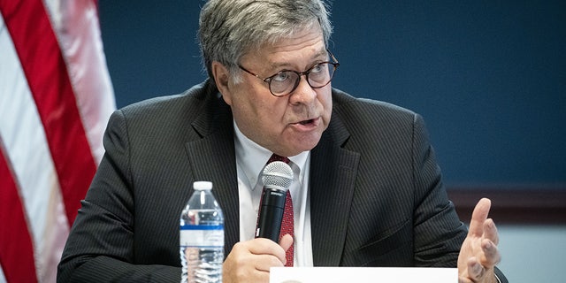 Bill Barr speaks into a mic, US flag behind him