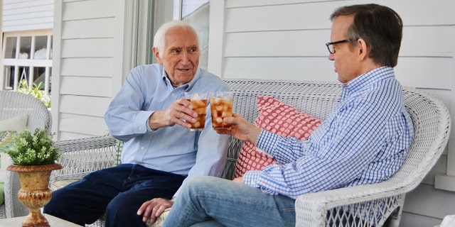 Gabe Briguglio and Eric Shawn wearing blue shirts cheers drinks on white couch outside