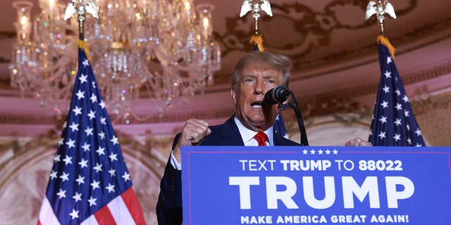 Donald Trump at lectern, chandelier, flags behind him