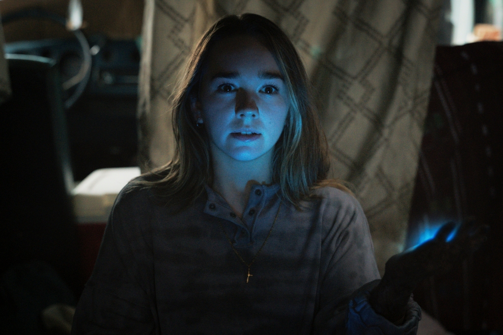 Shot of Holly Taylor as Angelina. She's in the dark with a blue glow on her face and emanating from her left hand. She's wearing a cross.