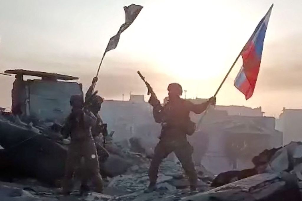 This video grab taken from a handout footage posted on May 20, 2023 on the Telegram account of the press service of Concord -- a company linked to the chief of Russian mercenary group Wagner, Yevgeny Prigozhin -- shows members of Wagner group waving a Russian national flag and Wagner Group's flag on the rooftop of a damaged building in Bakhmut