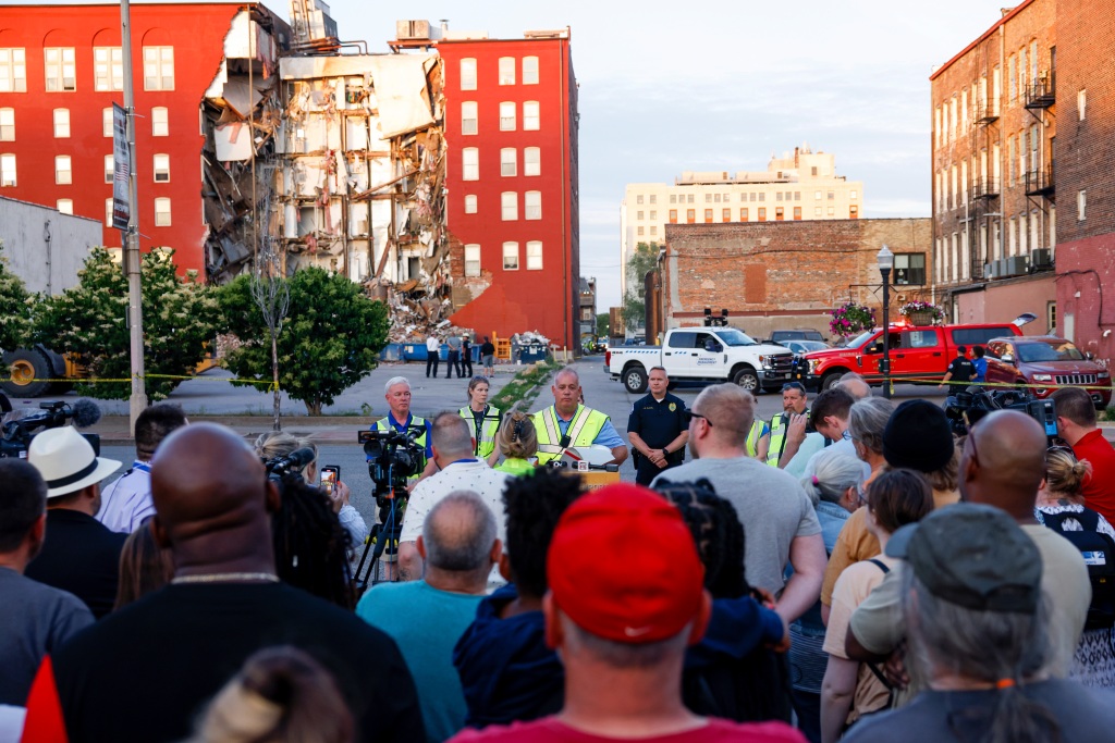 Officials update to media, residents and onlookers after a partial building collapse on the 300 block of Main Street, Sunday