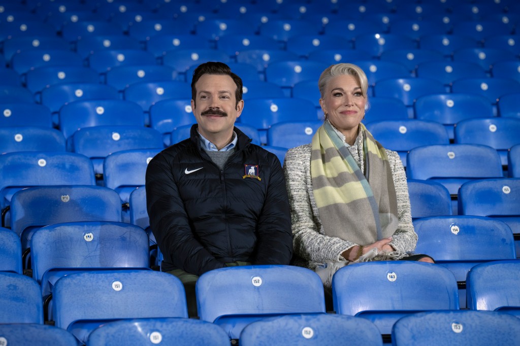 Ted Lasso (Jason Sudeikis) and Rebecca Welton (Hannah Waddingham) sit in the stands at Nelson Road.