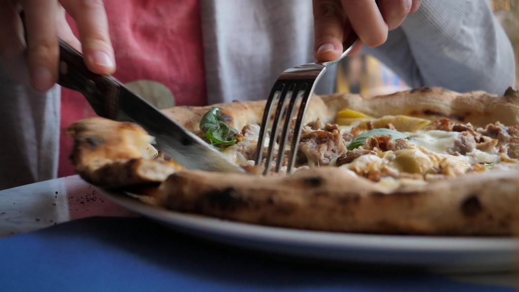 A fork and knife cutting pizza. 