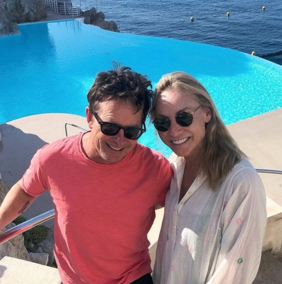 Michael J Fox with his wife smiling by a pool. 