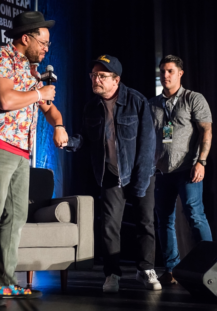 Michael J Fox walking on stage with another man behind him. 