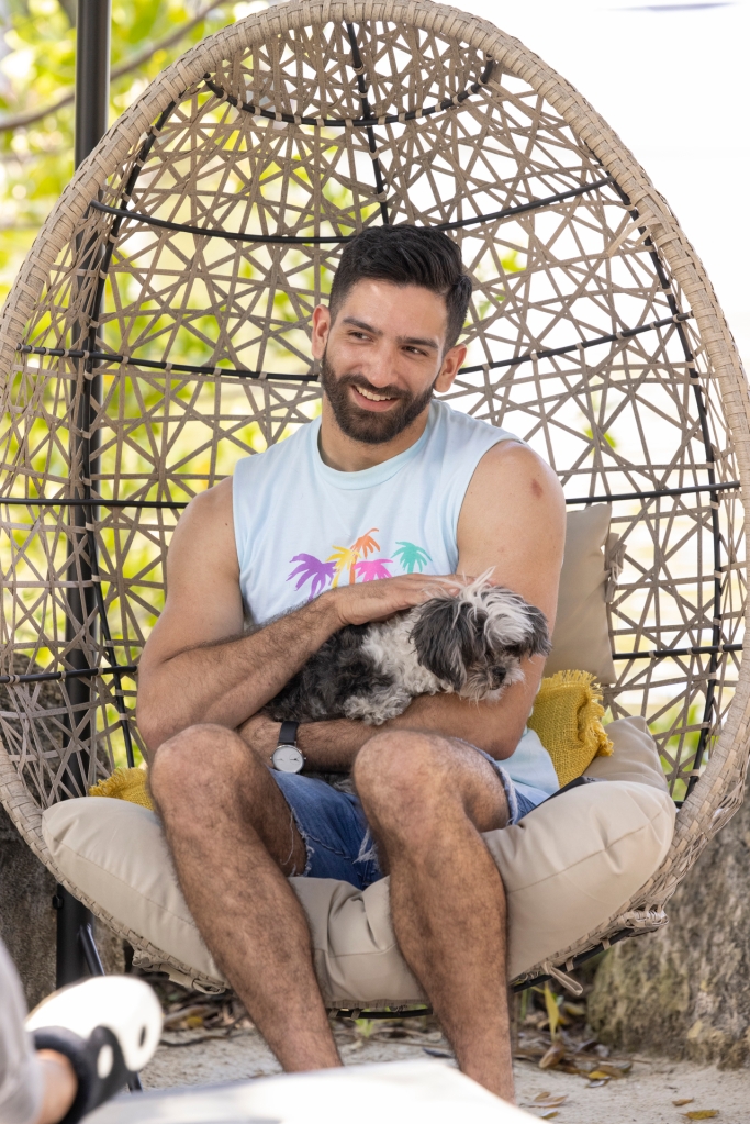 Kris sitting in a wicker chair with a dog, smiling. 
