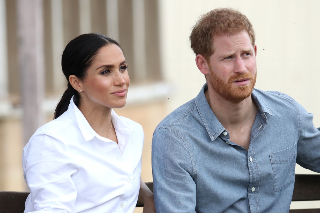 Harry and Meghan sitting next to each other looking serious. 
