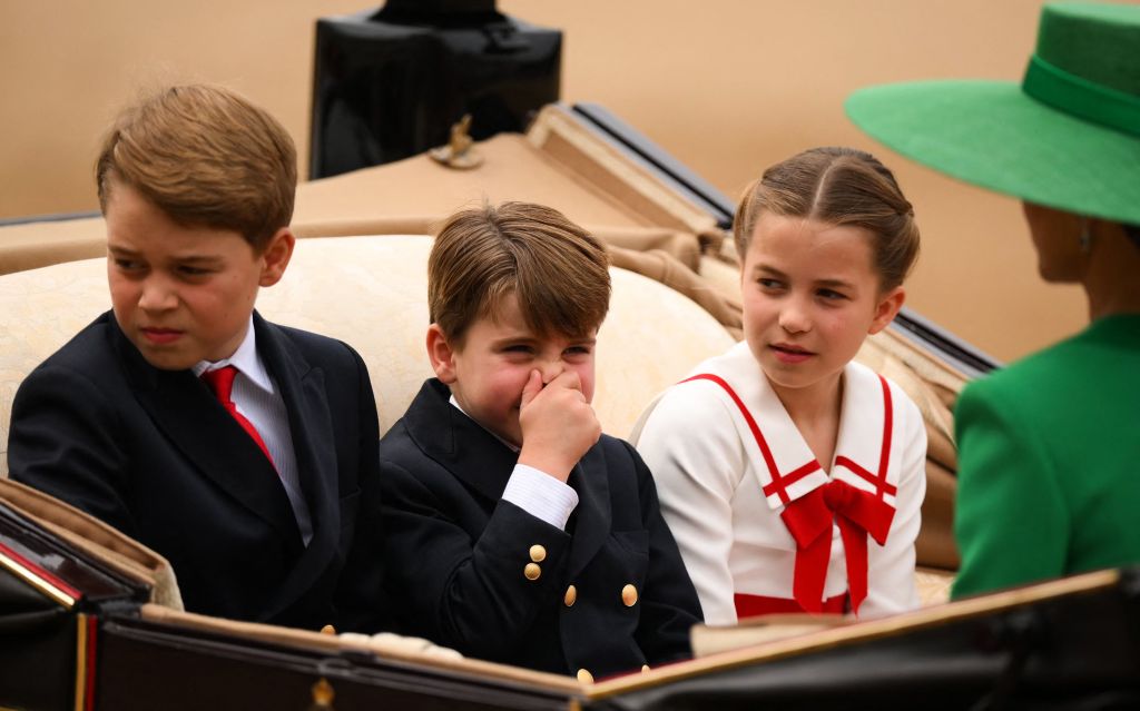 Prince Louis holds nose while seated in carriage next to siblings
