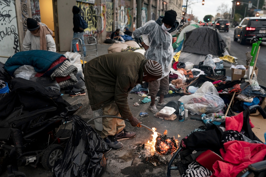 Robert Mason, a 56-year-old homeless man, warms up a piece of doughnut over a bonfire he set to keep himself warm on Skid Row in Los Angeles, on Feb. 14, 2023. 