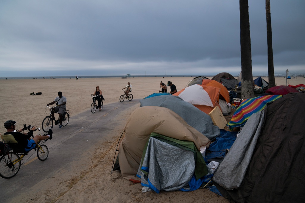  People ride their bikes past a homeless encampment set up along the boardwalk in the Venice neighborhood of Los Angeles on June 29, 2021. 