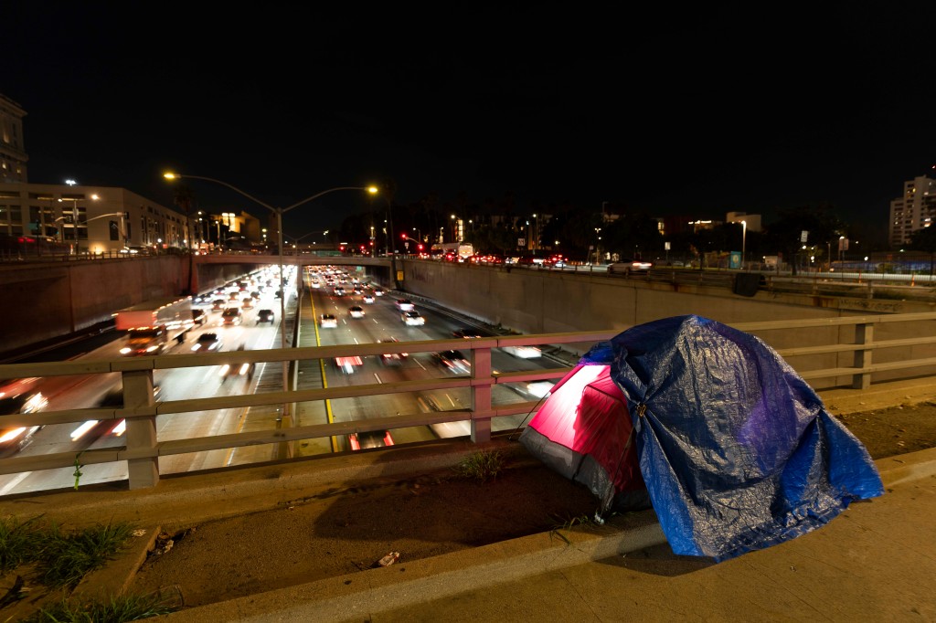 In this photo illuminated by an off-camera flash, a tarp covers a portion of a homeless person's tent on a bridge overlooking the 101 Freeway in Los Angeles, Thursday, Feb. 2, 2023.