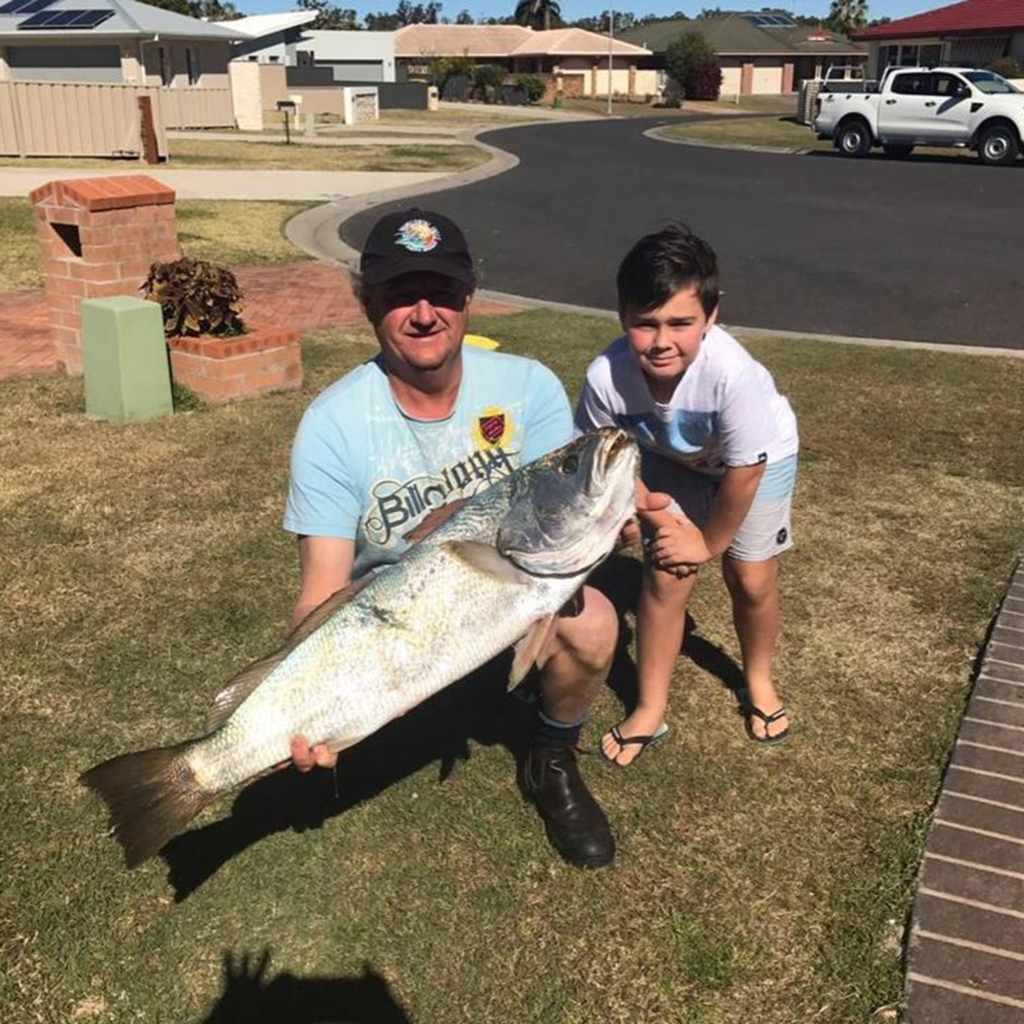 Noah stands next to his dad, who is holding up a large fish