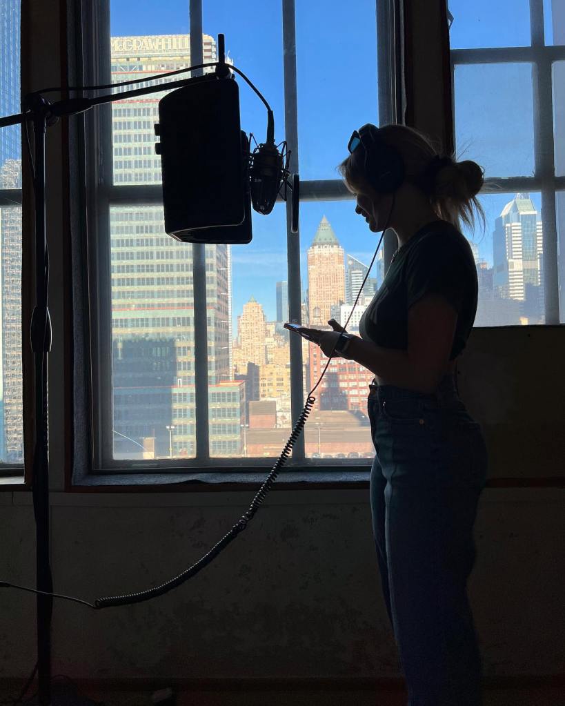 Alyssa McKay in silhouette next to a window overlooking New York City, while recording a podcast