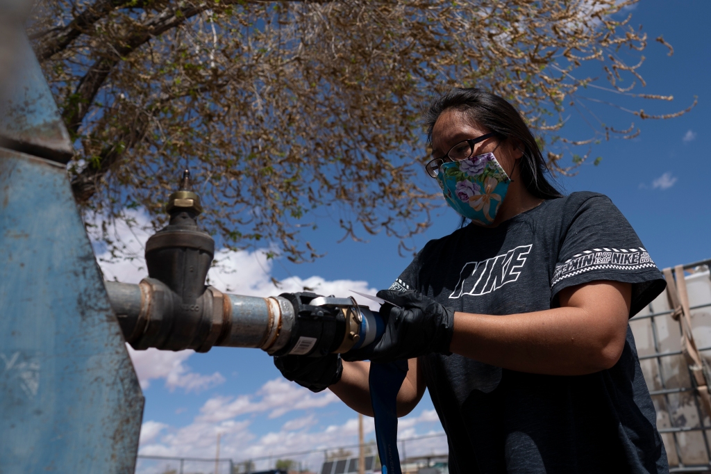 Raynelle Hoskie attaches a hose to a water pump to fill tanks in her truck outside a tribal office on the Navajo reservation in Tuba City, Arizona.