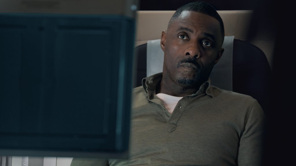Idris Elba sitting on a plane looking anxious. 