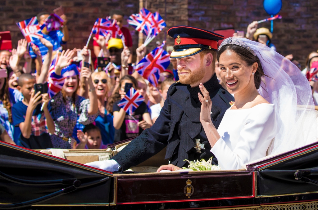 Harry and Meghan on their wedding day in a car smiling. 