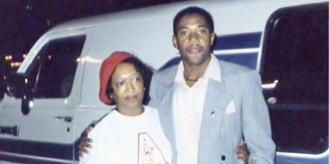 Minnie Smith wearing a white shirt and a red cap being held by her son