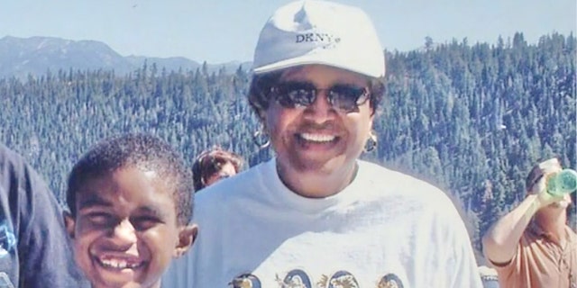 Minnie Smith wearing a white sweater and a white cap next to her grandson