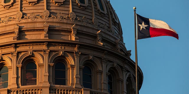 Texas Capitol building dome with the Texas flag waving in front.