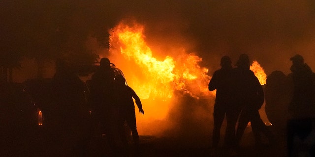 French rioters and police are hidden in shadow as a fire burns in the background during riots in Nanterre