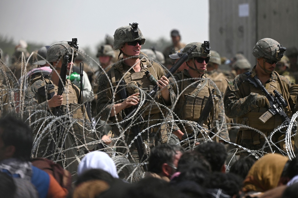 US soldiers stand guard behind barbed wire as Afghans sit on a roadside near the military part of the airport in Kabul on August 20, 2021.