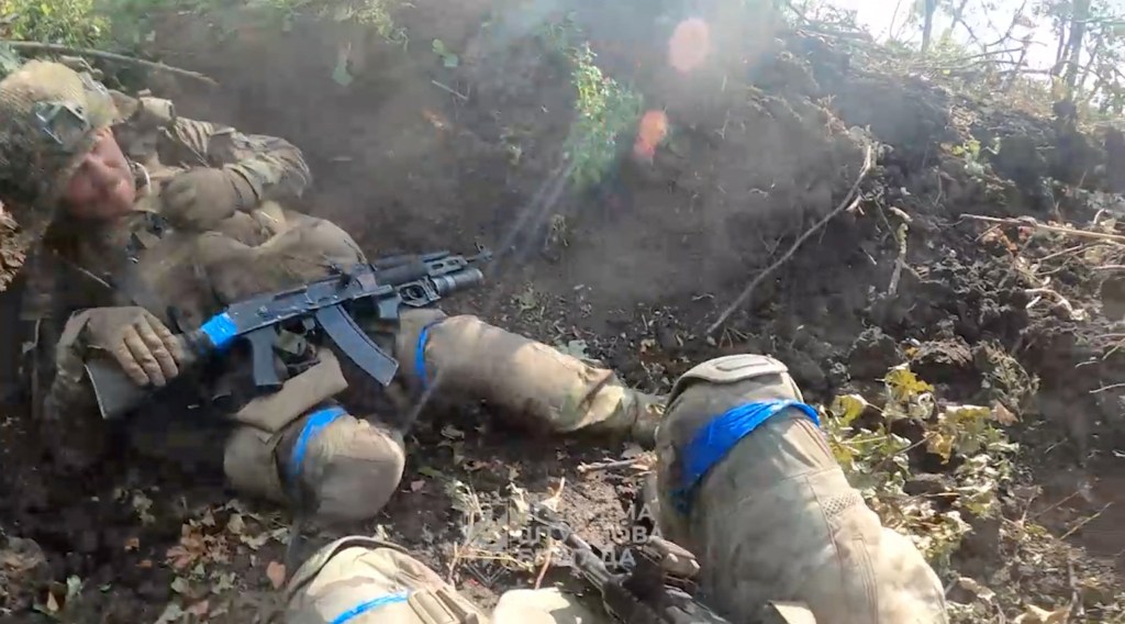Ukrainian soldiers take cover in a wooded area amid gunfire.