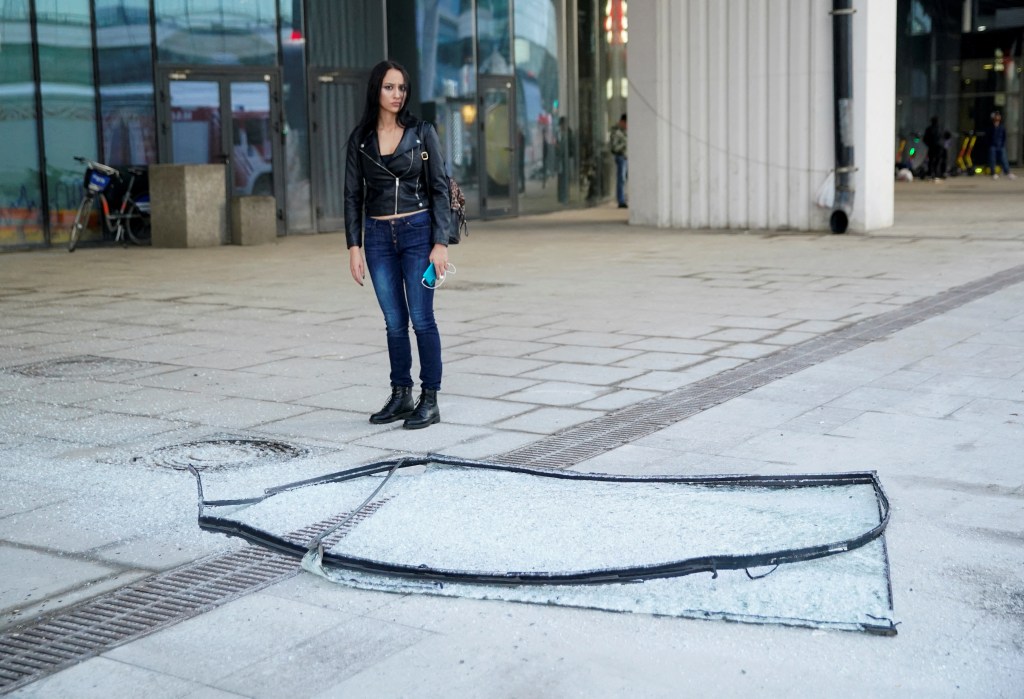 A woman stands next to a broken glass pane outside one of the office buildings that were damaged from the drone strike on Sunday.