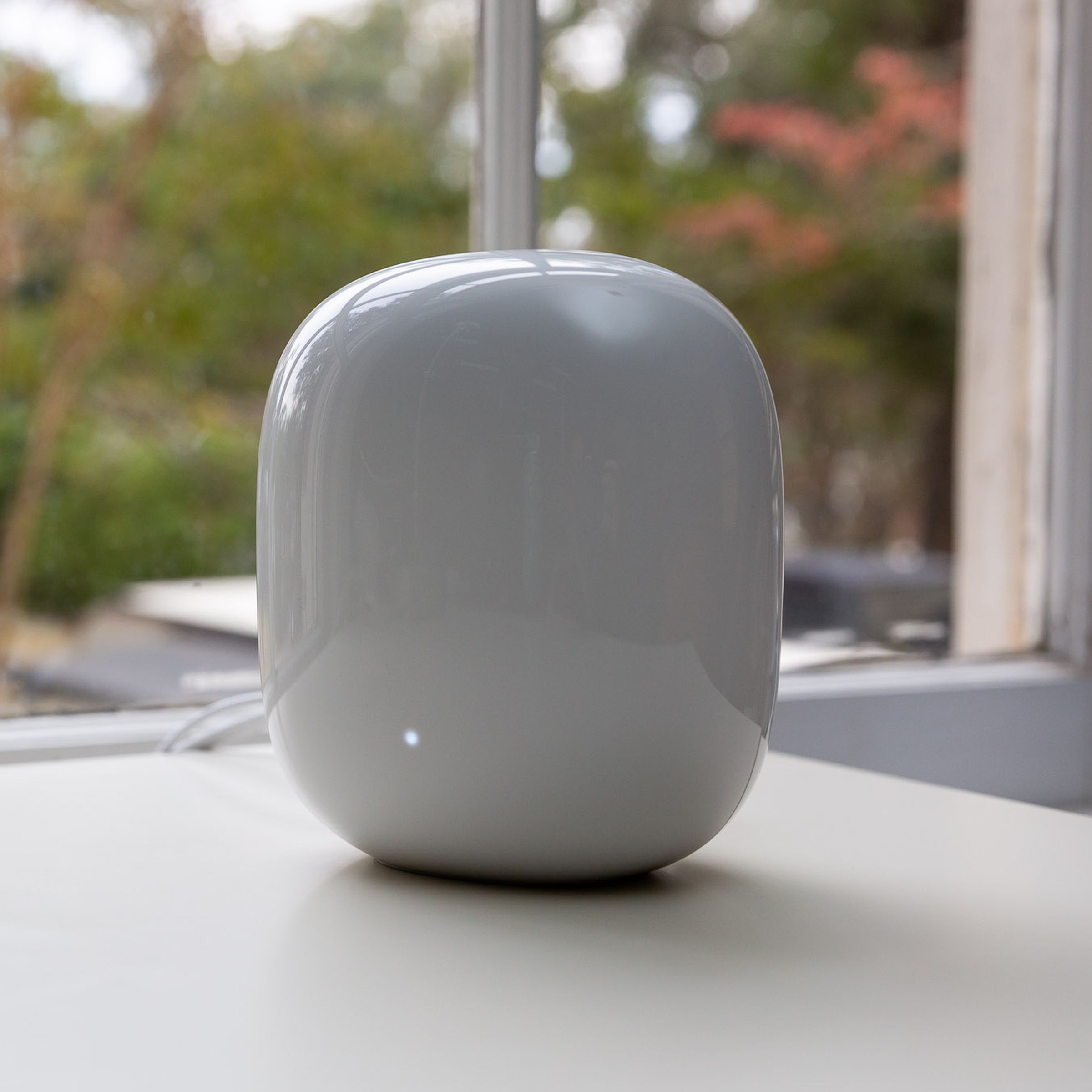 White Google Nest Wifi Pro router on a white table in front of a window.