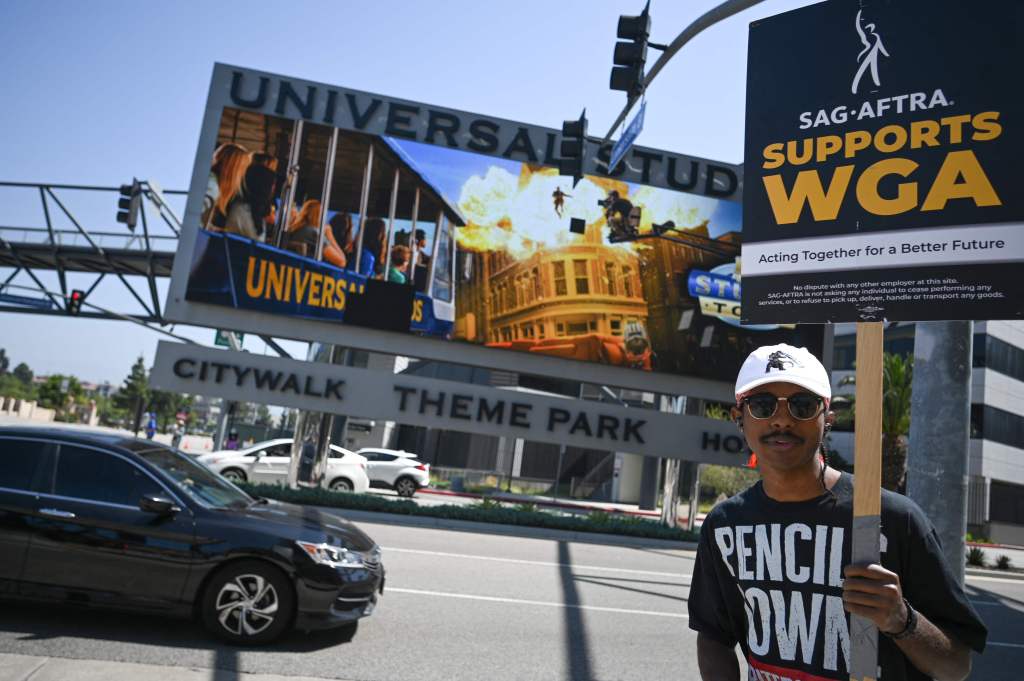 A supporter holds a "SAG AFTRA Supports WGA" sign outside Universal Studios Hollywood in Los Angeles, Calif., on June 30, 2023.