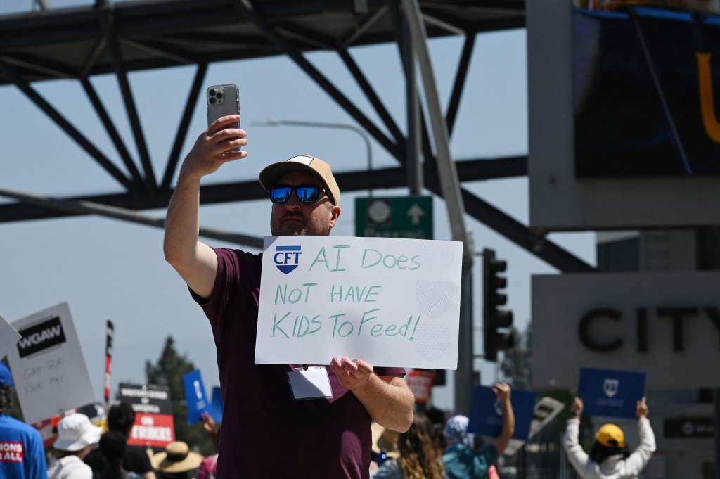 A teacher supporting striking Hollywood writers holds up a sign reading "AI Does Not Have Kids to Feed!" on the picket line outside Universal Studios Hollywood in Los Angeles, Calif., on June 30, 2023. 