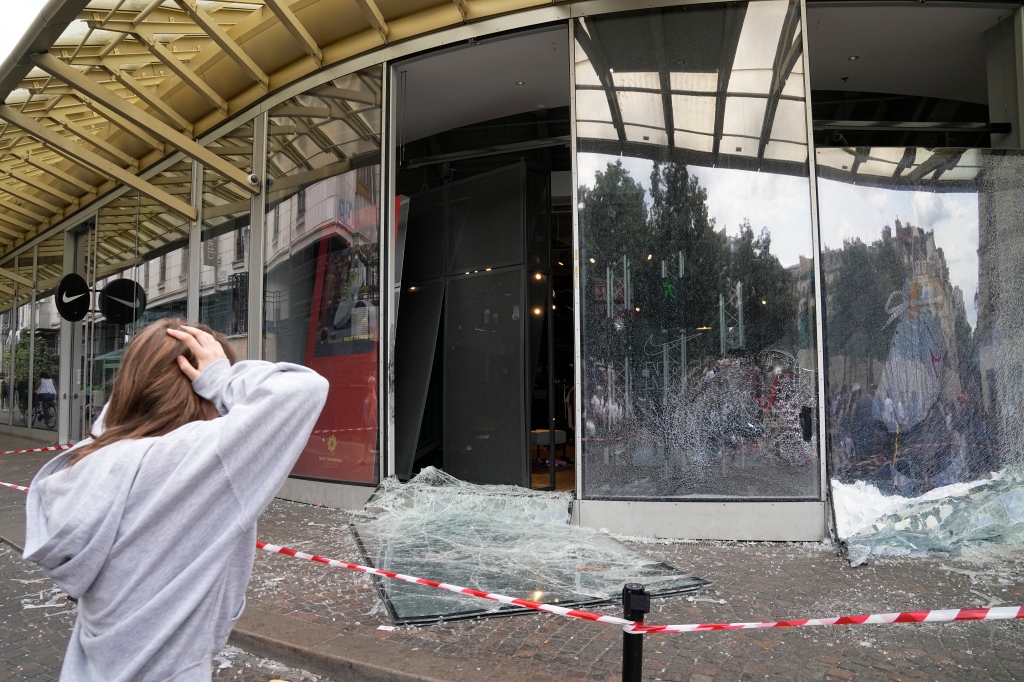 A woman reacts by damaged sports store after a third night of unrest, Friday, June 30, 2023 in Paris.