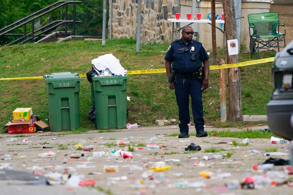 A police officer stands in the area of a mass shooting incident in the Southern District of Baltimore, Sunday, July 2, 2023. Police say a number of people were killed and dozens were wounded in a mass shooting that took place during a block party just after midnight.