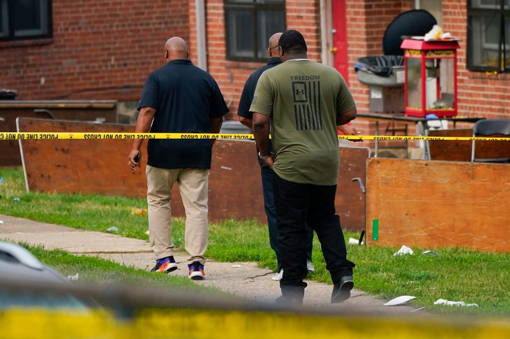 Members of the Baltimore Housing Authority walk near tables left on their side in the area of a mass shooting incident 