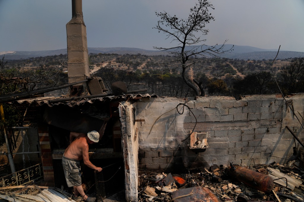 An owner of a burnt house tries to clean after yesterday's fire in Mandra west of Athens, on July 19, 2023.