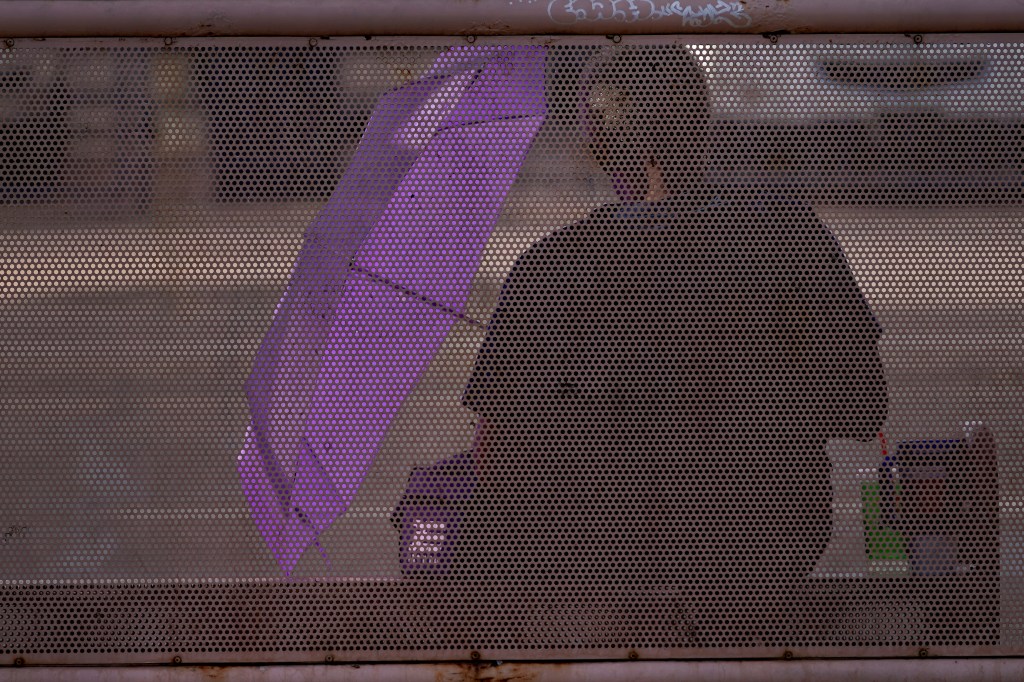 A man uses an umbrella to block the sun at a bus stop amid a heat wave on July 30, 2023, in Phoenix. 