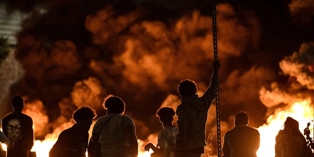 Protesters stand in front of flames